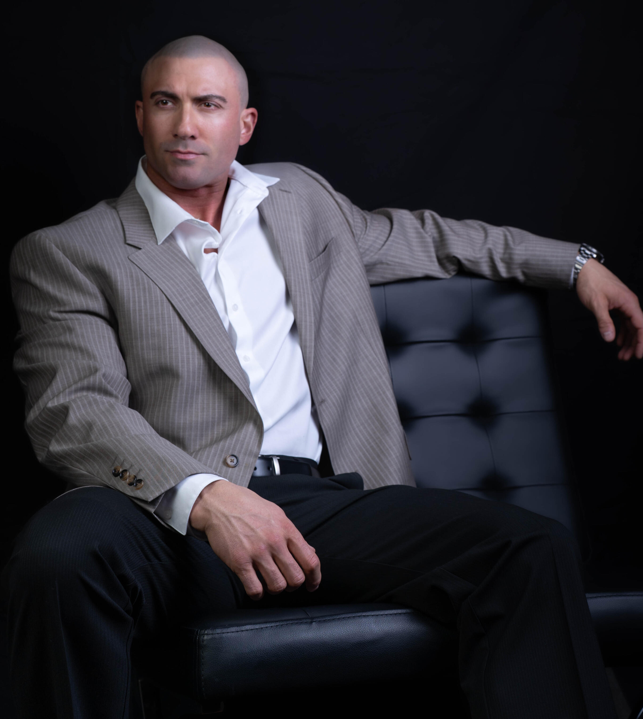 Professional photo of Thomas Rooney - former headline performer, author, and entrepreneur wearing a suit, sitting in a Barcelona chair
